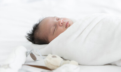 Adorable newborn baby wrapped in white swaddle towel lying on bed and sleeping peacefully with...