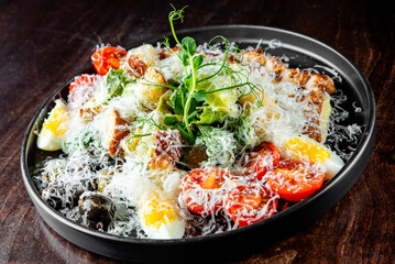 A fresh Caesar salad with grilled chicken, cherry tomatoes, eggs, and parmesan on a dark plate
