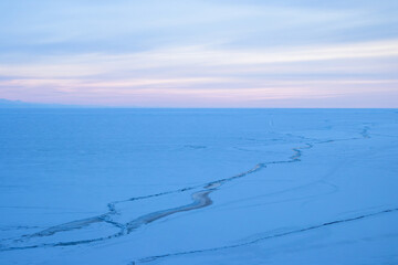 Ice-covered Lake Baikal. Winter landscape. The beginning of evening twilight after sunset. Cracks are visible on the surface of the ice. Cold weather. January, winter. Siberia, Russia.