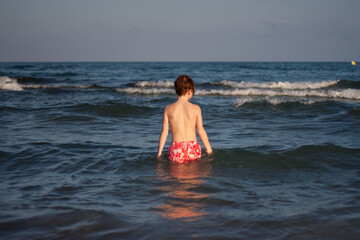 portrait of redhead boy from behind with red swimsuit looking at the sea. Horizontal. copy space	
