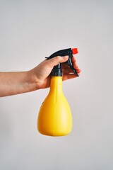 A young woman holds a spray bottle in her hand. Yellow spray bottle on white background. High quality photo