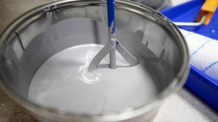 The installer carefully mixes gray paint in a plastic bucket to apply it to the walls. Concept of...