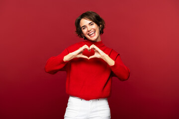 Portrait photo of joyful, attractive woman making a heart gesture with her hands
