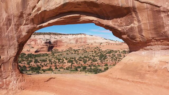 Aerial flies through rock arch in orange stone massive of cliff formation. Red mountains Usa Utah. Erosion and rainfall have formed arches in soft sandstone rock. Popular place tourists to visit