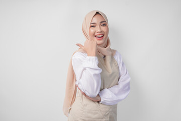 Excited young Asian Muslim woman in hijab and cream apron pointing to the empty copy space on the...