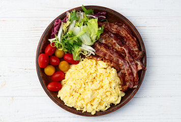 Breakfast plate . Scrambled eggs , bacon , cherry tomatoes and salad