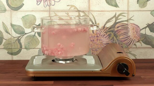 Boiling pink tapioca pearls in a transparent glass pot over a gas stove, an ingredient for bubble tea