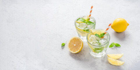 Two glasses of lemonade adorned with ice, lemon slices, and fresh mint leaves, evoking a refreshing...