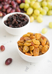 Bowls of green and red dark raisins with ripe raw grapes on light background.Macro.
