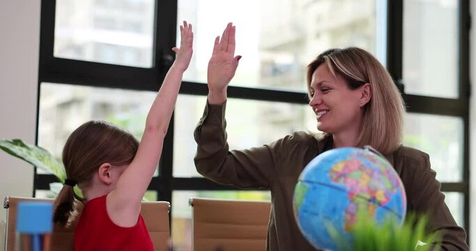 Little girl and teacher giving high five in classroom near globe 4k movie slow motion. Friendly attitude towards children at school and kindergarten concept