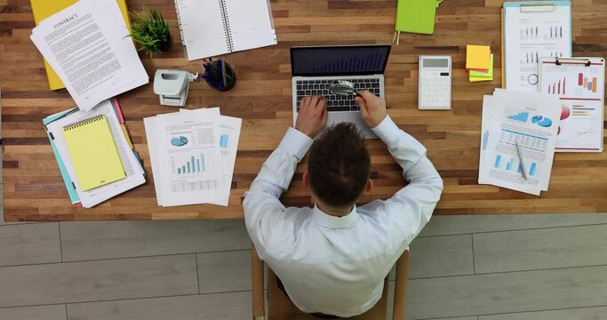 Businessman studying graph on laptop with magnifying glass at table in office top view 4k movie. Profit growth strategy in business concept