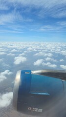 View from an airplane window with engine and blue sky clouds.