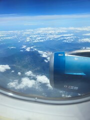 View from an airplane window with engine and blue sky clouds.