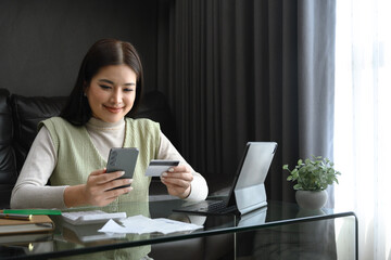 Satisfied young adult woman holding credit card and smartphone at home