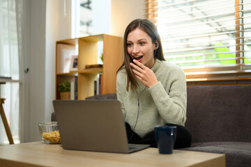 Shocked young woman watching horror on laptop and covering her mouth by hand