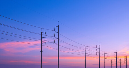 Silhouette two rows of electric poles with cable lines on roadside against colorful orange sunset...