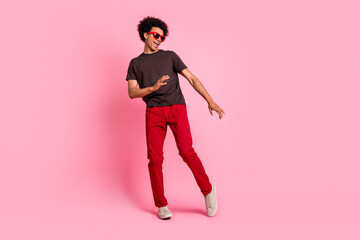 Full body length photo of millennial curly hair man dance in eyewear brown t shirt and red pants...