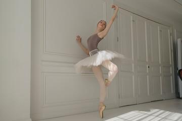 ballerina in a light bodysuit and tutu stands against the wall showing elements of ballet