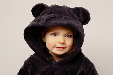 child in a suit. little beautiful girl sitting on a light background in a brown bear costume, outfit concept