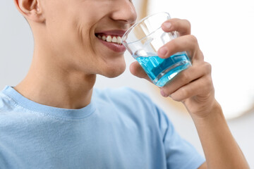 Young man using mouthwash indoors, closeup view