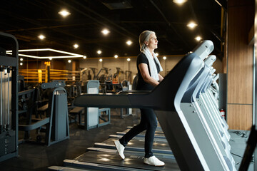 attractive athletic senior woman in sportswear exercising actively on treadmill while in gym