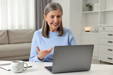 Happy woman having video chat via laptop at table indoors