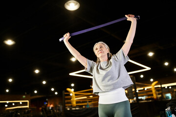 merry mature good looking sportswoman in cozy attire training with fitness expander while in gym