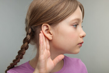 Little girl with hearing problem on grey background, closeup