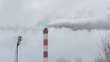Thermal power plant smokes against the backdrop of a cityscape on a cloudy day