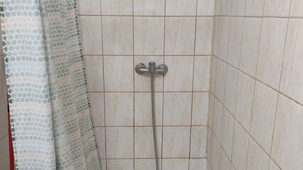 Old dirty tiled bathroom with shower and dirty floor in a cheap hostel or student dormitory