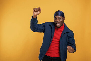 Naklejka premium Having fun, celebrating success, hands up. Handsome black man is in the studio against yellow background