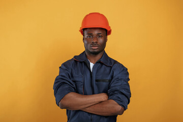 In orange hard hat. Construction worker. Handsome black man is in the studio against yellow background