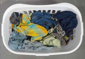 Closeup overhead shot of wet washed laundry, consisting of colored clothing and other fabrics, in a white plastic basket, ready to be dried.
