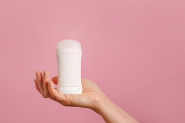 Female hand holding white deodorant on pink background. Closeup. copy space