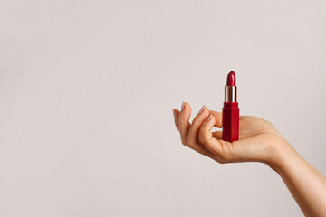Woman hand holding red lipstick on light background, copy space