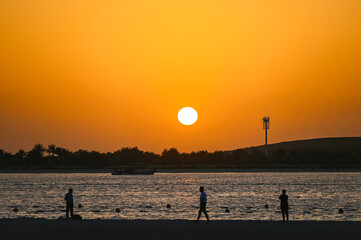 People walking along Corniche Beach in Abu Dhabi during warm evening with sunset in  United Arab Emirates