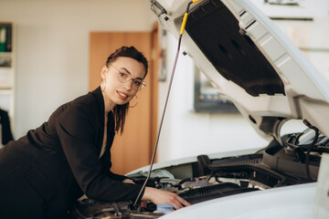 a woman looks under the hood of a car in a car dealership