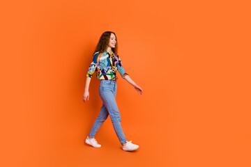 Photo of adorable optimistic girl wear trendy print clothes going empty space isolated on vivid orange color background