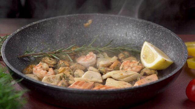 Professional chef prepares shrimps, salmon and mussels on pan. Cooking seafood, healthy vegetarian food on a vegetables background.