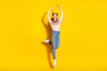 Photo portrait of pretty young woman jump dance ballet raise hands dressed stylish knitted warm outfit isolated on yellow color background