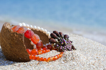 Pearls, amber and jewelry on the sand against the background of the blue ocean.