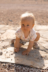 Beautiful little blonde girl in shorts and a T-shirt plays on the beach, happy sunny spring day