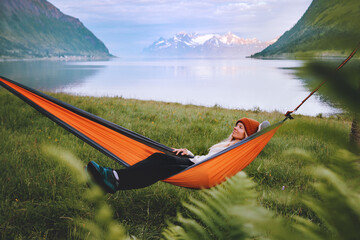 Traveler woman chilling in hammock travel lifestyle summer vacations trip in Norway girl relaxing outdoor enjoying fjord and mountains view harmony with nature eco tourism - obrazy, fototapety, plakaty