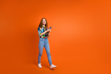 Photo of cheerful cute girl user dressed stylish clothes hold iphone going empty space isolated on orange color background
