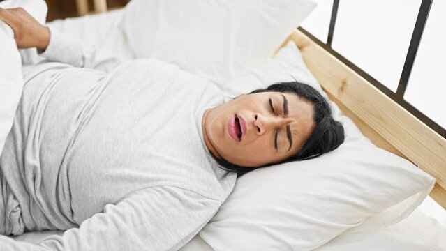 A middle-aged hispanic woman appears distressed while lying in bed, suggesting insomnia or illness in a cozy bedroom setting.