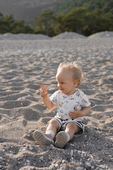 Beautiful little blonde girl in shorts and a T-shirt plays on the beach, happy sunny spring day