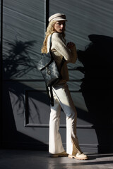 Studio portrait of beautiful woman with a curly blond hair holding brown bag, posing on gray background.