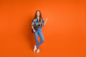 Fototapeta na wymiar Photo of cheerful adorable girl wear trendy clothes recommend modern device empty space isolated on vivid orange color background