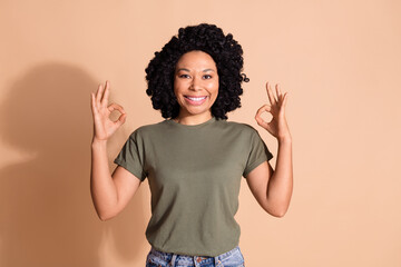 Photo of optimistic woman with perming coiffure wear khaki t-shirt showing okey approve nice work isolated on beige color background