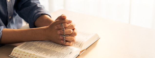 Asian male folded hand prayed on holy bible book while holding up a pendant crucifix. Spiritual,...